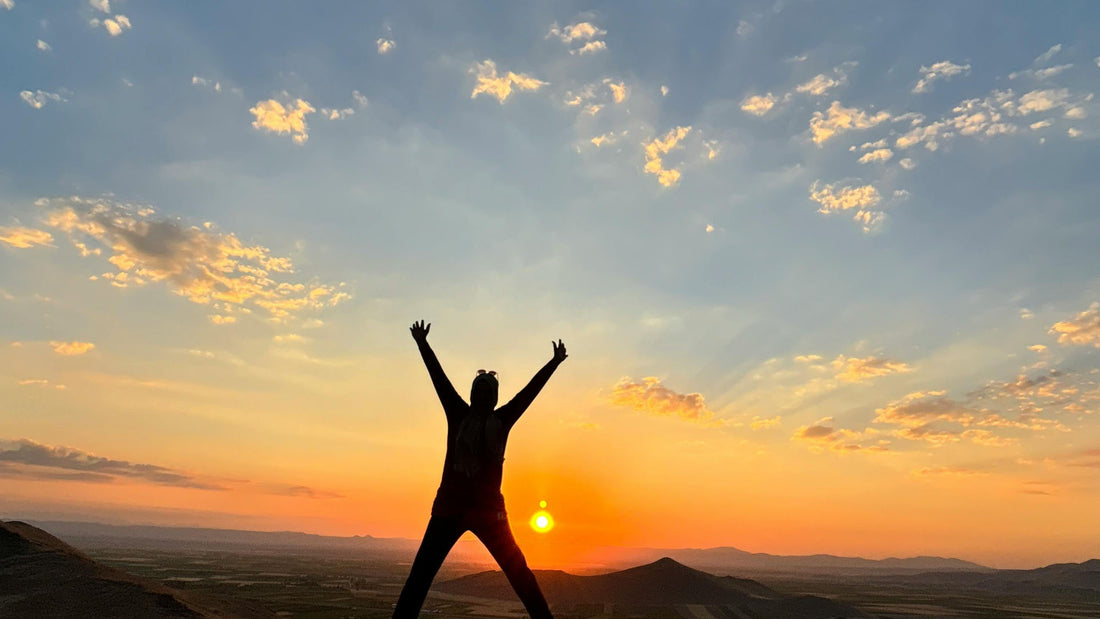 silhouette of a person celebrating at sunset on mountain peak