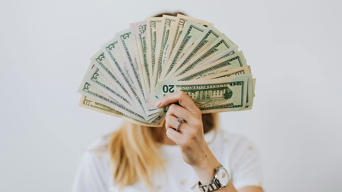 person holding a fan of cash that's covering their face