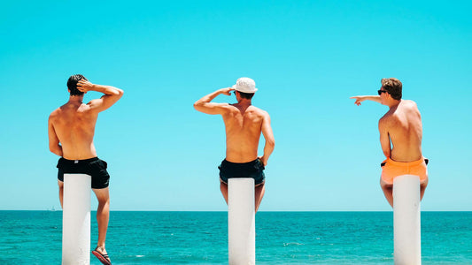 three men sitting on white concrete near the beach during daytime