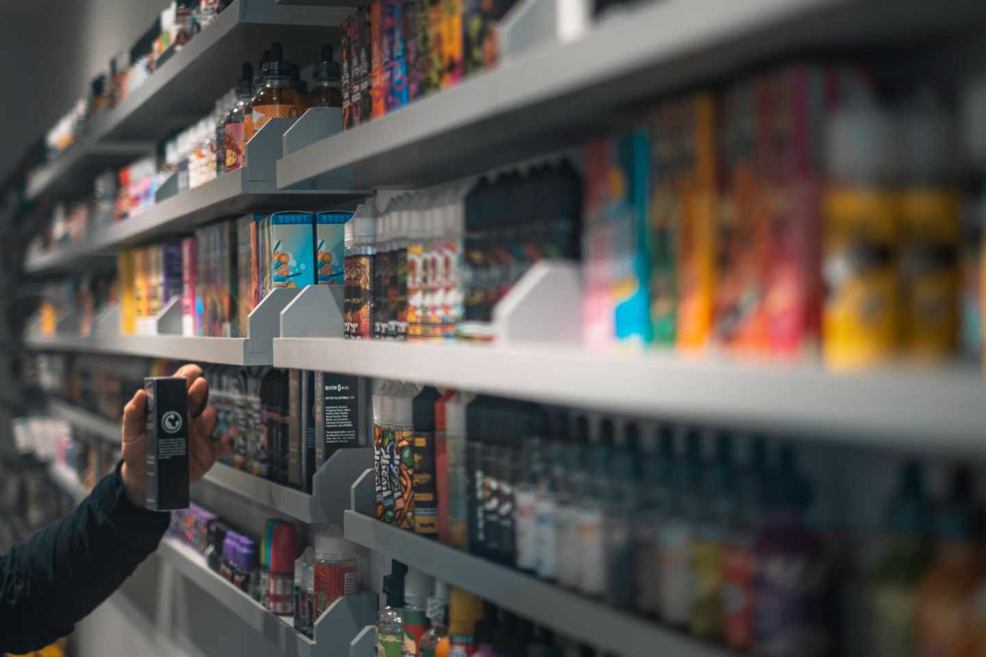 A wall of vape juices on shelves, a hand is taking an item off the shelf.