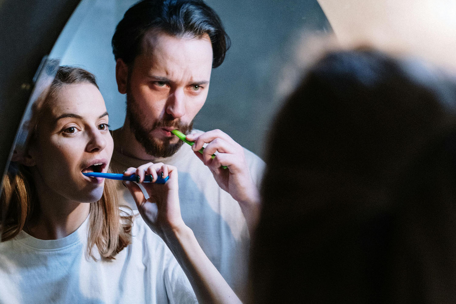 couple brushing their teeth together in front of a bathroom mirror