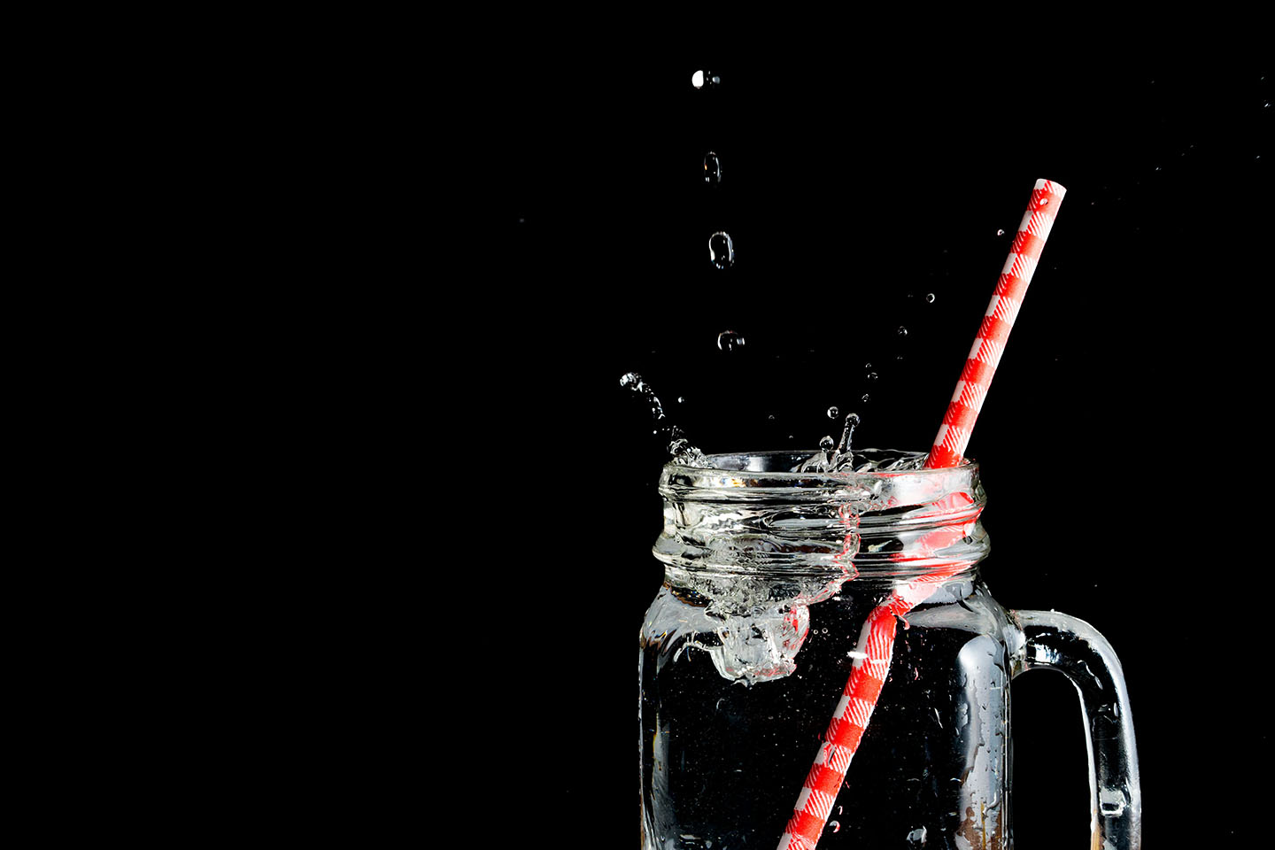 glass of water with straw against black background