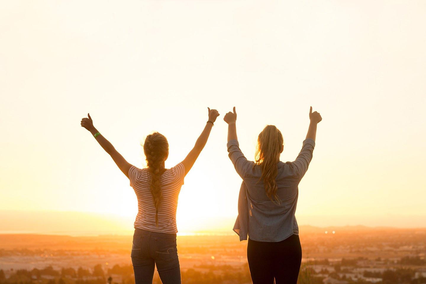 two women with arms raised looking at landscape during daylight