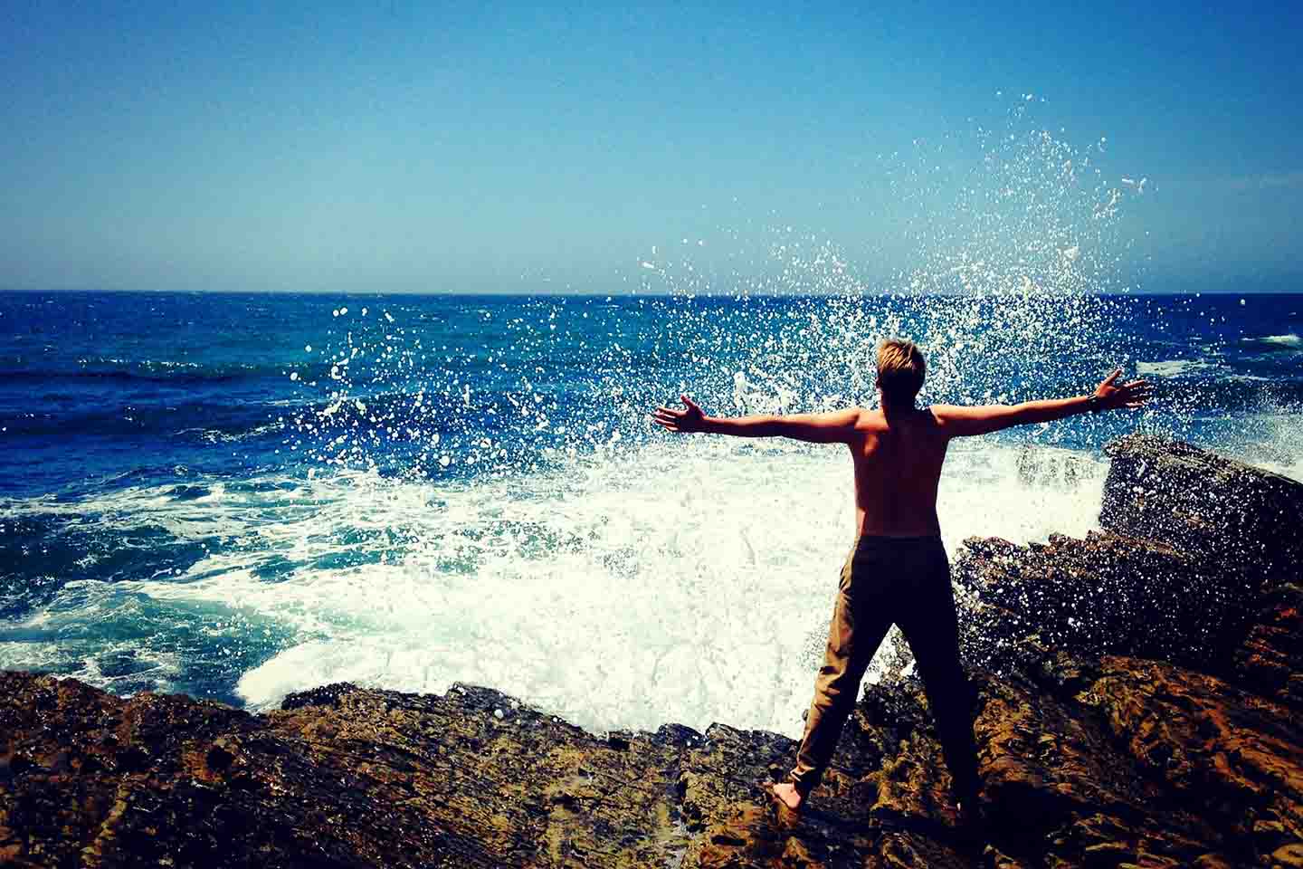 man standing on rocks looking at the ocean with arms outstretched