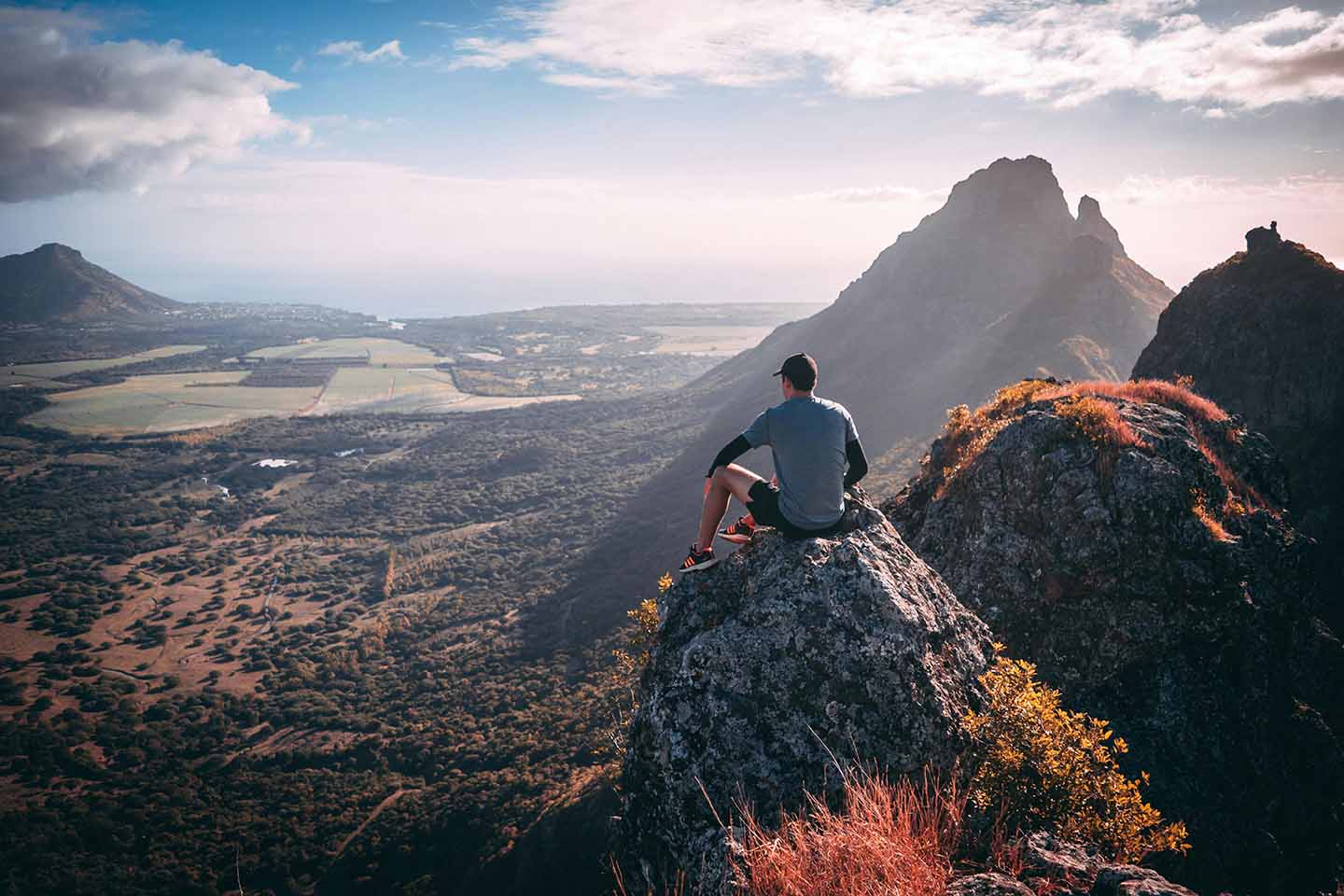 Man sitting on top a mountain overlooking a valley
